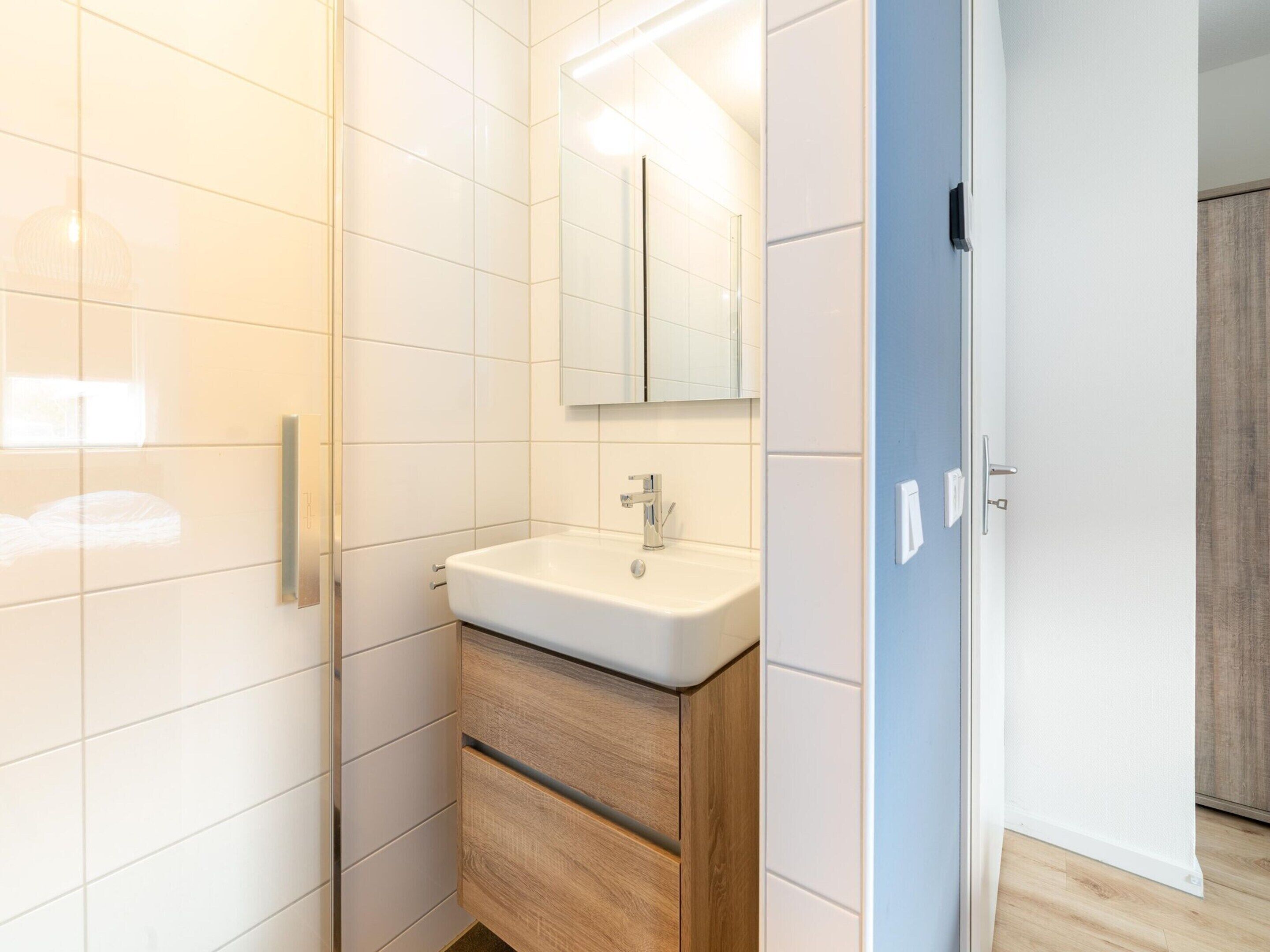 A modern bathroom with a white sink, wooden cabinet, and a mirror above it.