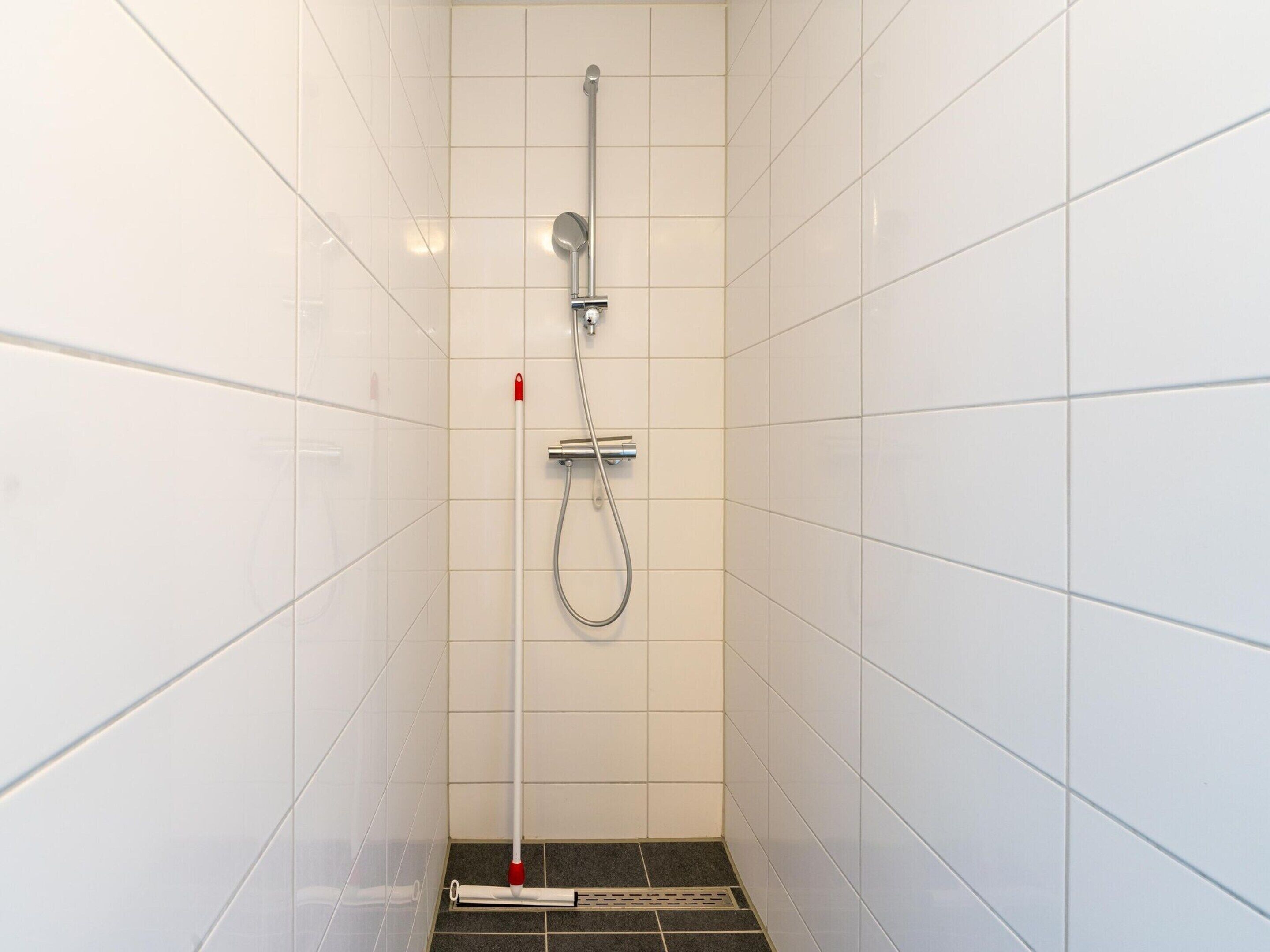 A small, tiled shower stall with a handheld showerhead and a handheld shower attachment.