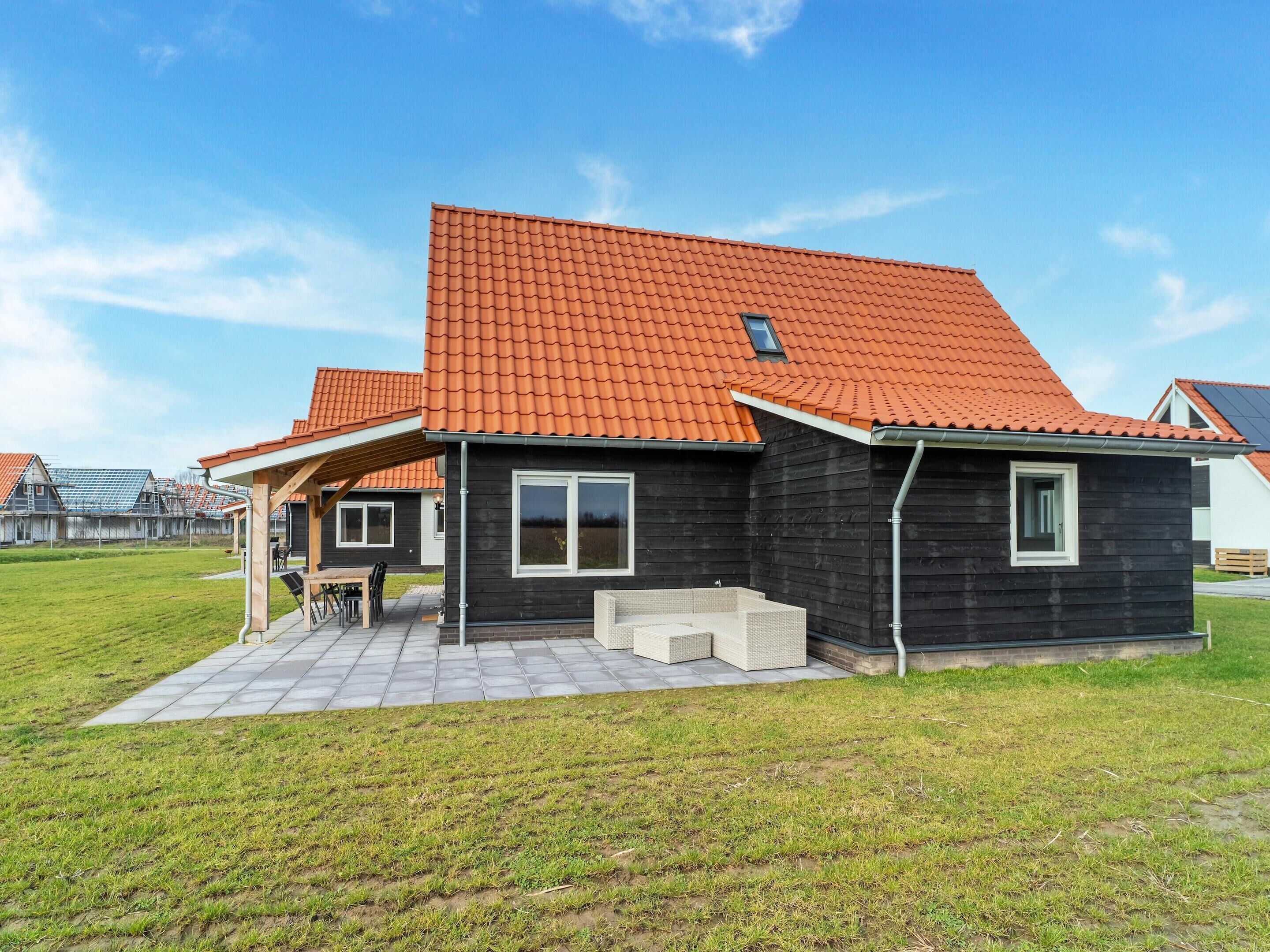 Ein modernes Haus mit Ziegeldach, überdachter Terrasse und gepflegtem Rasen.