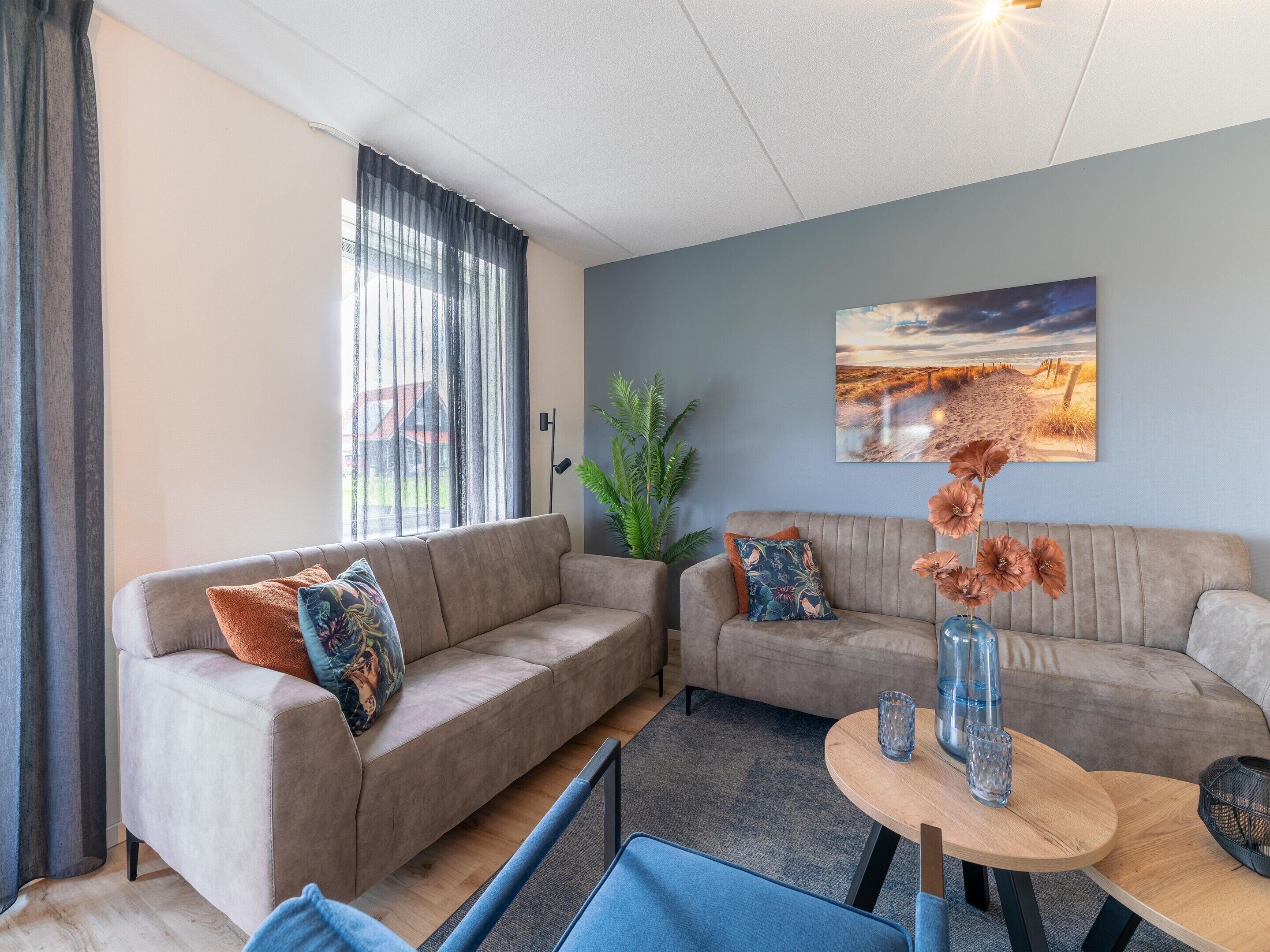 A modern living room with two sofas, a coffee table, and a large window with sheer curtains.