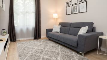 Een moderne woonkamer met een grijze bank, een kamerkleed met dessin, een lamp en lijstwerken aan de muur.
