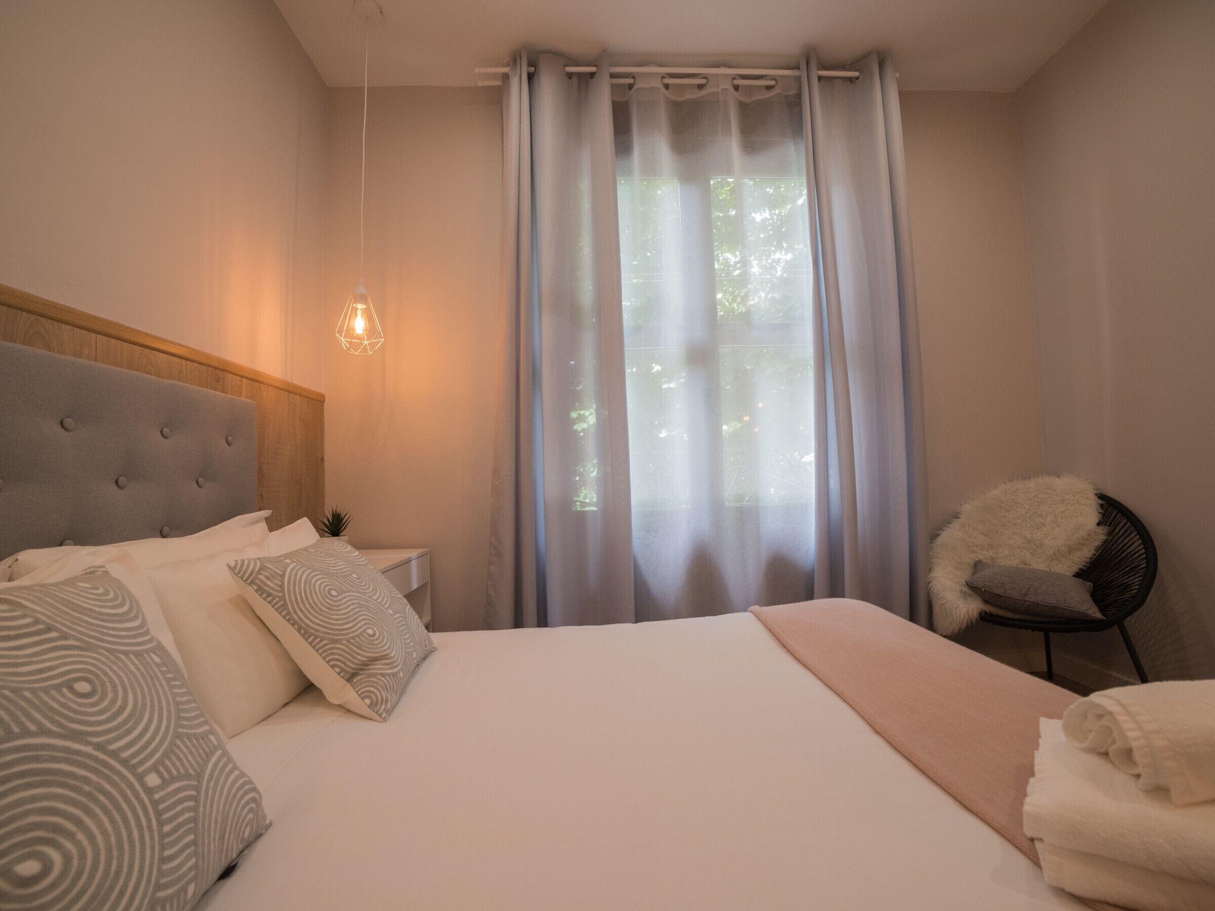 Une chambre à coucher avec un grand lit, une table de chevet, une chaise et une fenêtre avec des rideaux.