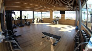 Una palestra con pavimenti in legno, diverse attrezzature per esercizi e ampie finestre con vista sull'esterno.
