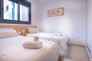A hotel room with two beds, a window, a wall-mounted artwork, and a bedside lamp.