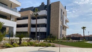 Un edificio moderno con diversi balconi, una vasca idromassaggio e un'area verde con palme.