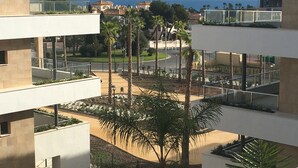 Un edificio moderno con numerosi balconi che si affacciano su un'area verdeggiante con palme e vista sul mare.