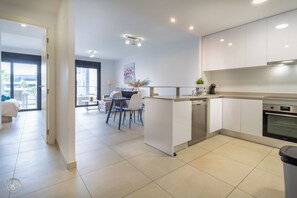Una cocina moderna con armarios blancos, horno empotrado y comedor con mesa y sillas.