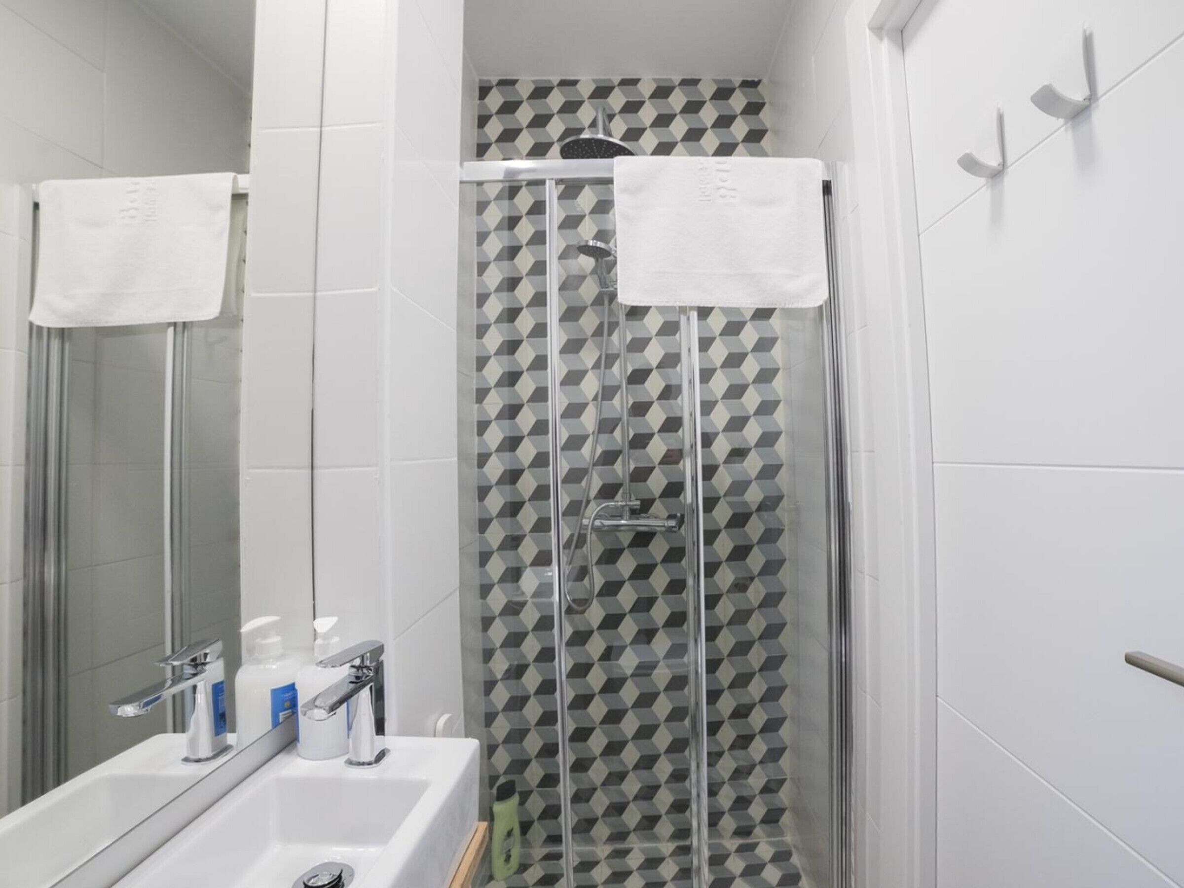 A modern bathroom with a glass shower enclosure, a white sink with a mirror, and a geometric-patterned shower wall.