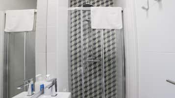 A modern bathroom with a glass shower enclosure, a white sink with a mirror, and a geometric-patterned shower wall.