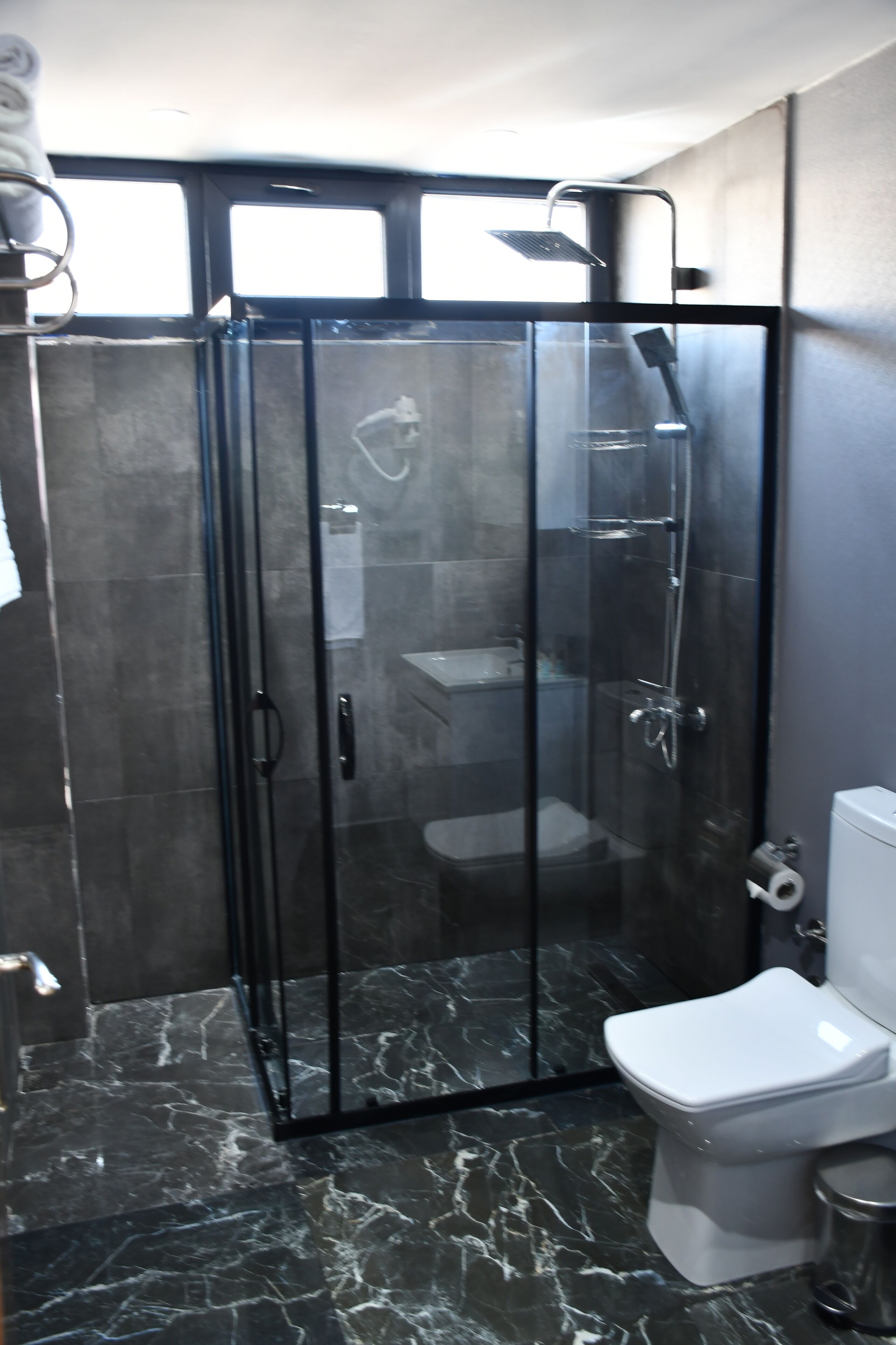 A modern bathroom with a glass-enclosed shower, a toilet, and a marble floor.