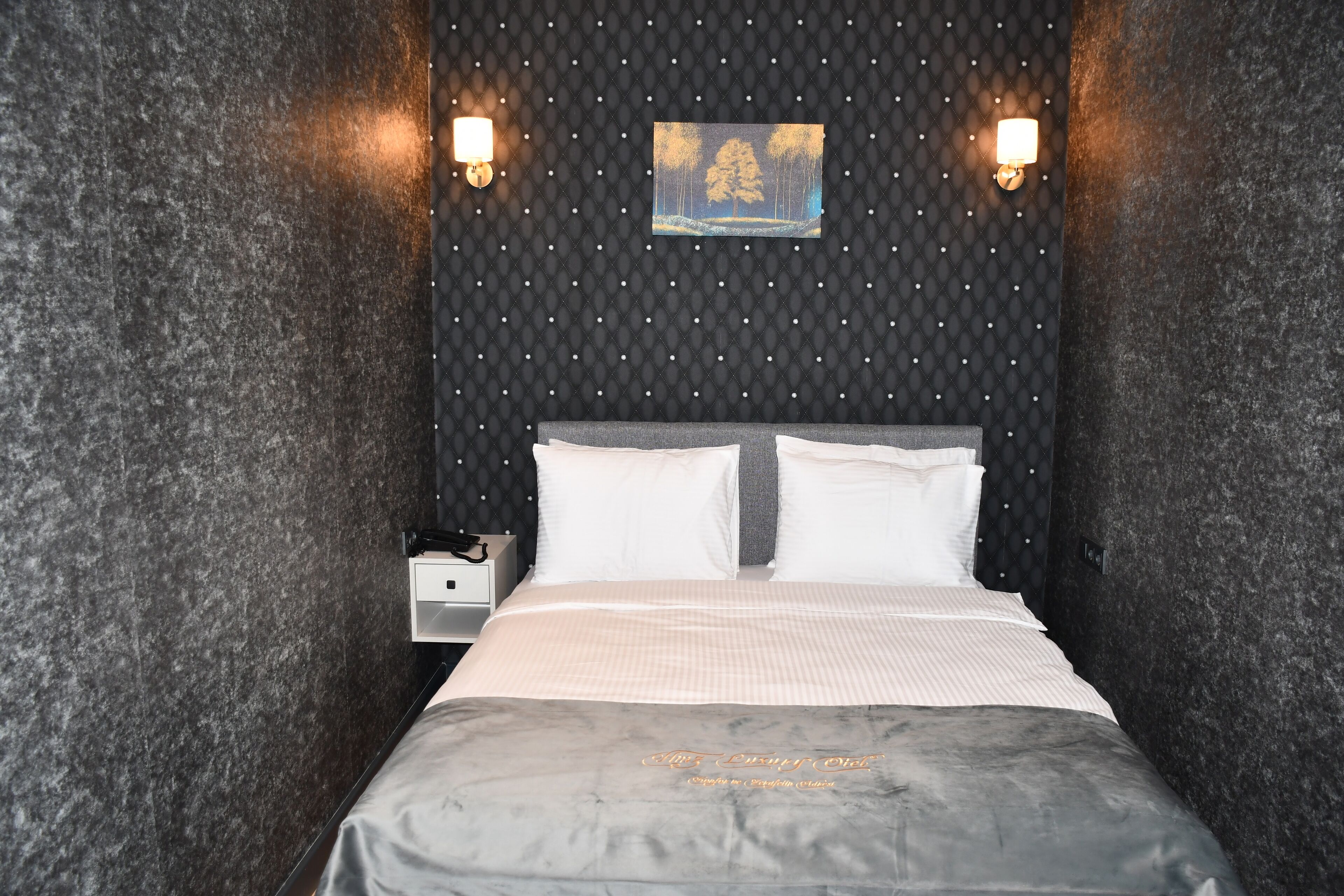 A room with a bed, two wall-mounted lights, a small bedside table, and a framed picture on the wall.