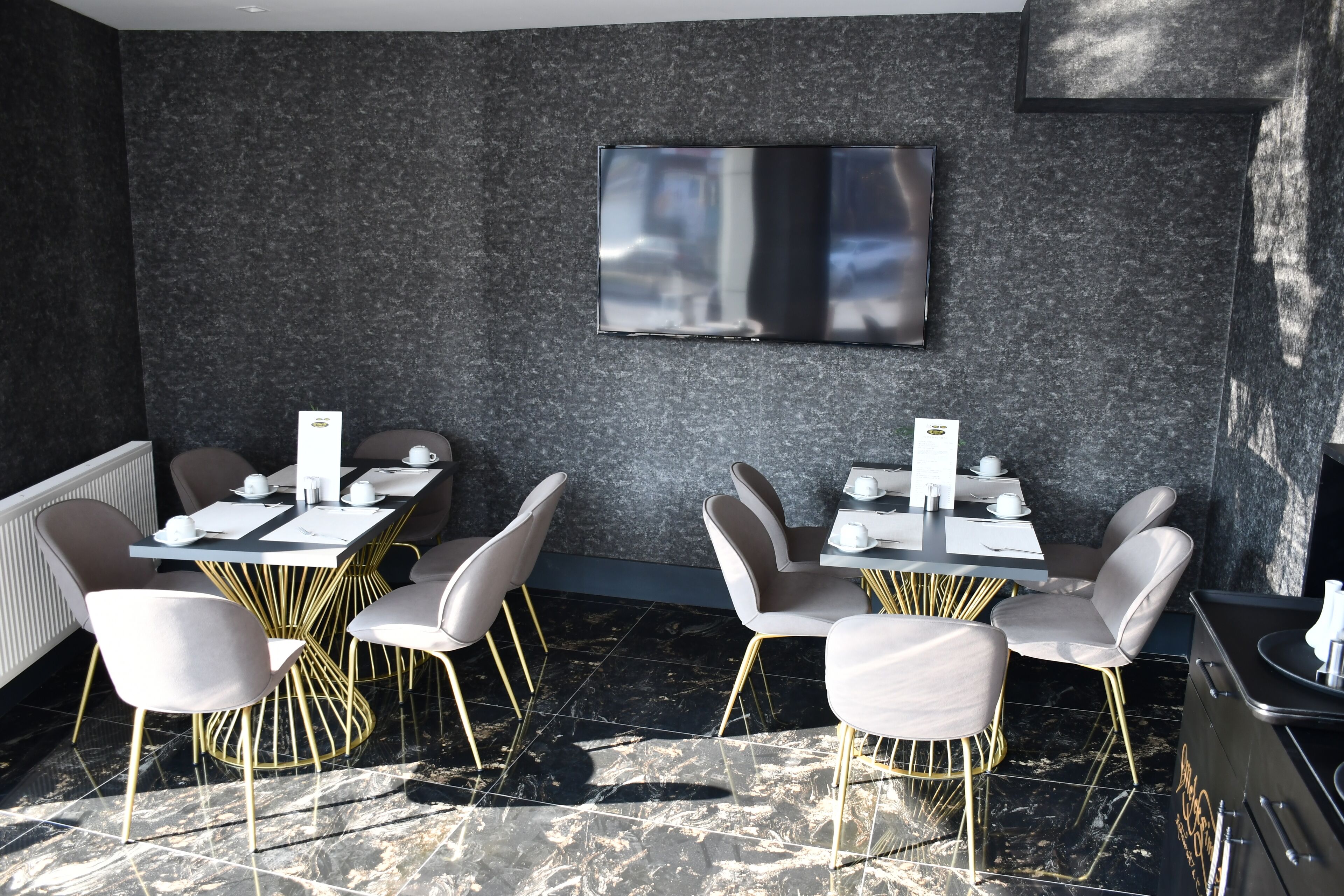 A modern dining area with marble flooring, gold-trimmed tables, and white chairs.