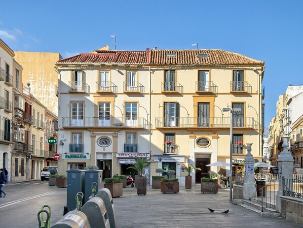 Un edificio de varios pisos con techo de tejas, varios balcones y locales comerciales, incluyendo una farmacia y un restaurante.