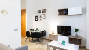 A modern living room with a TV, a dining table with chairs, and a sofa. - Historic Málaga Apt: Quiet Retreat w/ Courtyard, 4-min Walk to Larios (Málaga)