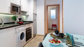 A compact kitchen with a washing machine, microwave, and a small dining area with a table and chairs. - Historic Málaga Apt: Quiet Retreat w/ Courtyard, 4-min Walk to Larios (Málaga)