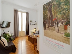 A modern living room with a flat-screen TV, a sofa, a coffee table, and a large poster on the wall. - Charming 1-Bedroom Apartment in Málaga Center with Balcony and Courtyard (Málaga)
