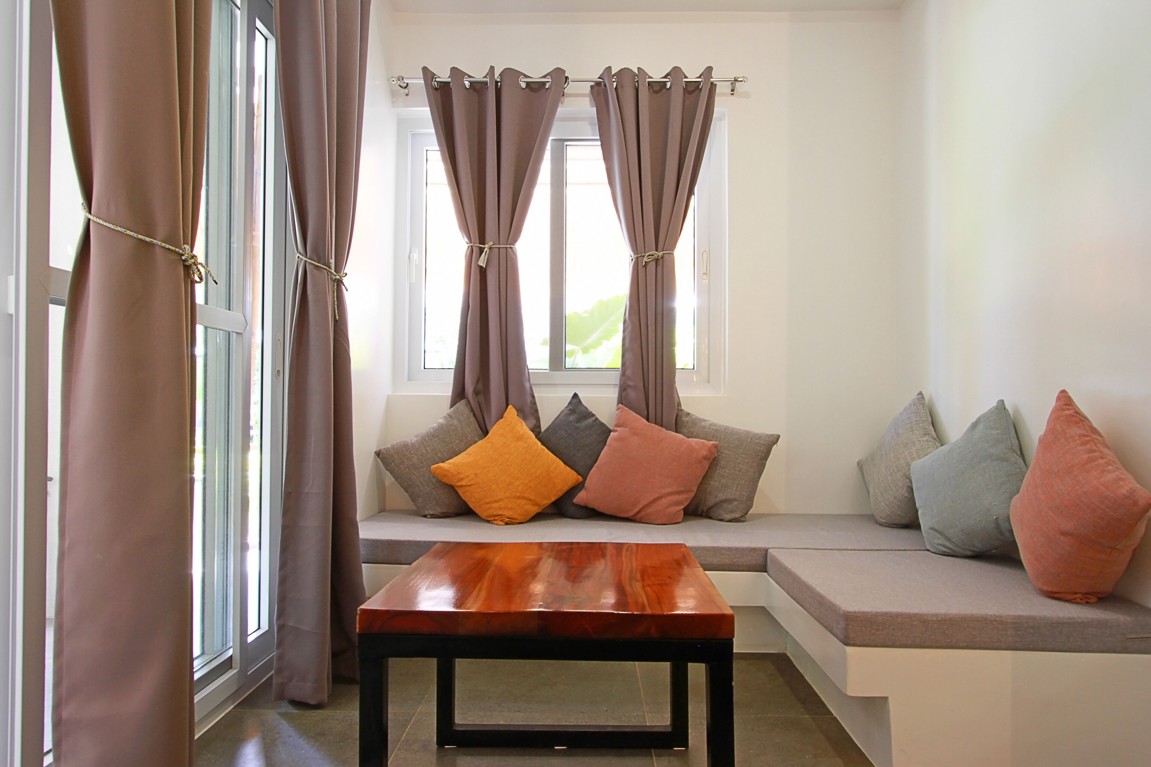 A room with a window, curtains, a bench, and cushions.