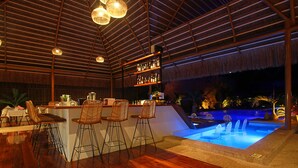 Un espace bar doté d’un plancher en bois, de tabourets de bar et d’une piscine éclairée de lumières bleues.