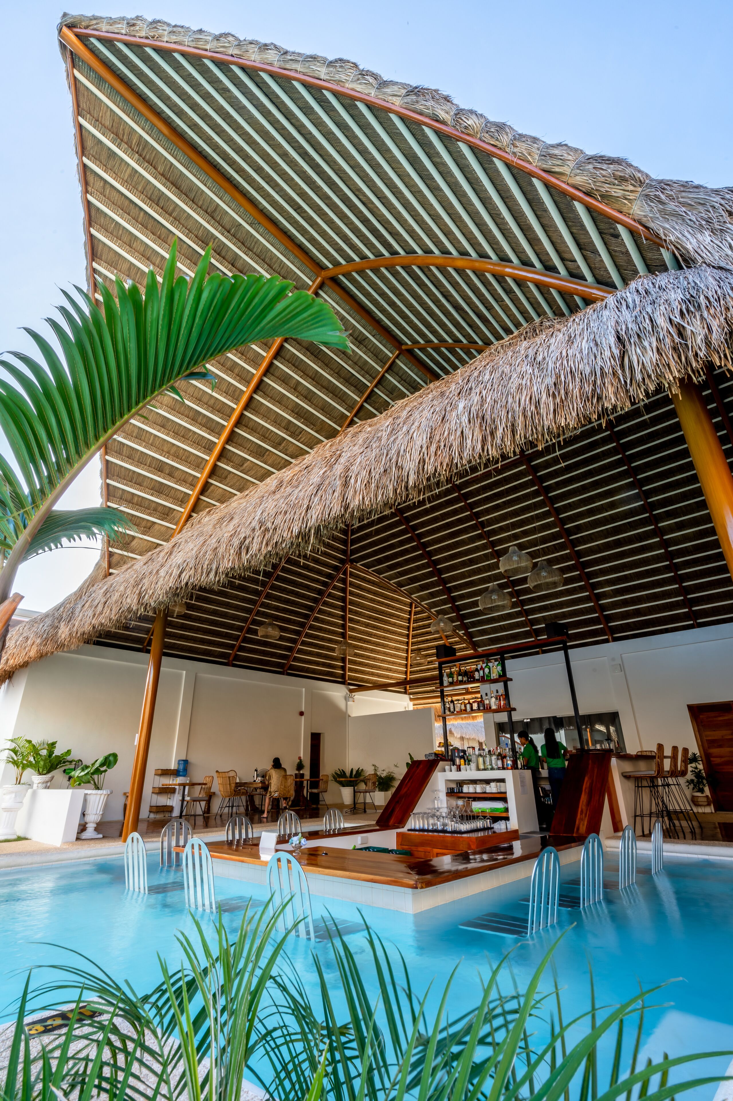 A pool area with a thatched roof, lounge chairs, and a bar.