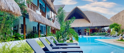 A resort with thatched-roof buildings, a swimming pool, and lounge chairs.