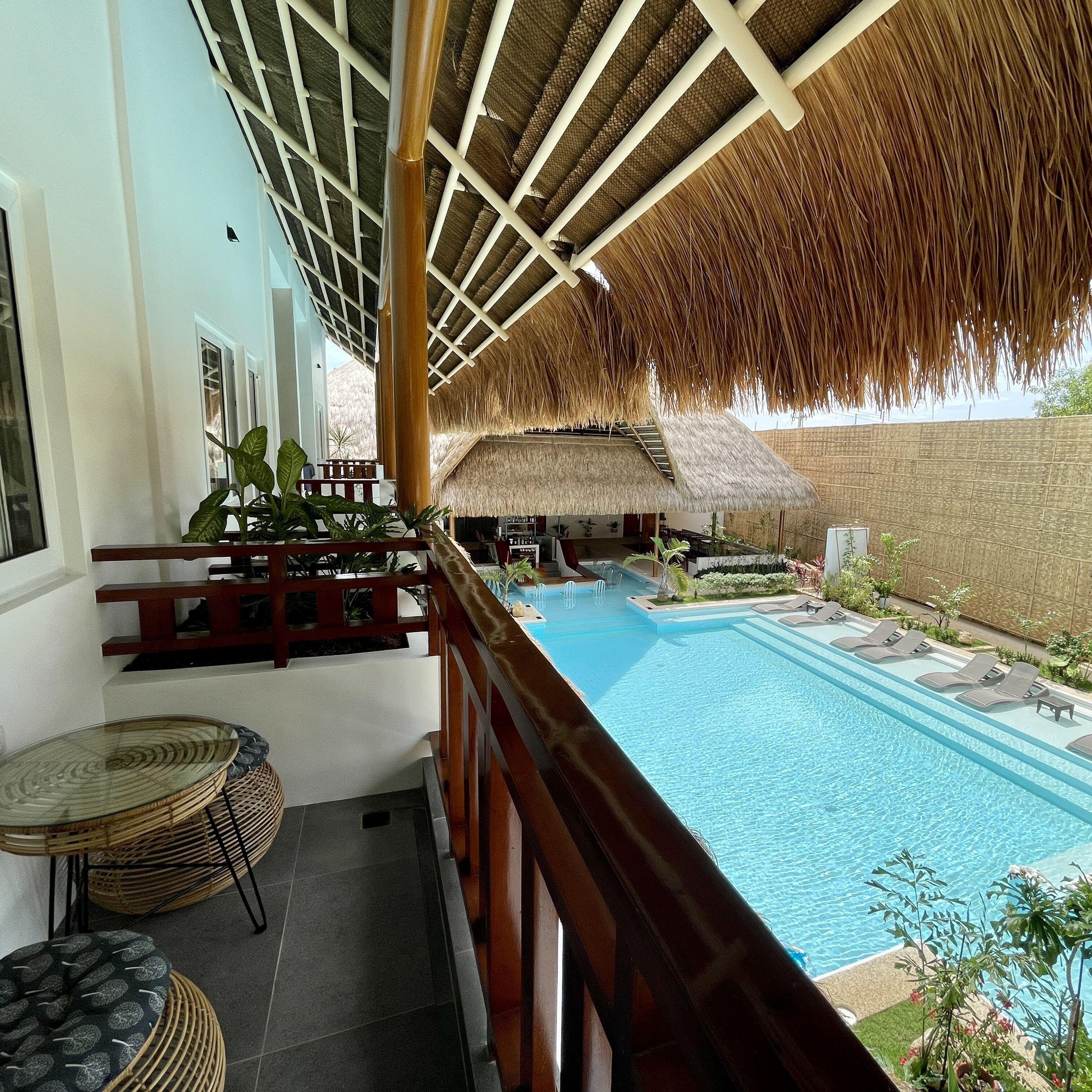 A pool area with a thatched roof, lounge chairs, and potted plants.
