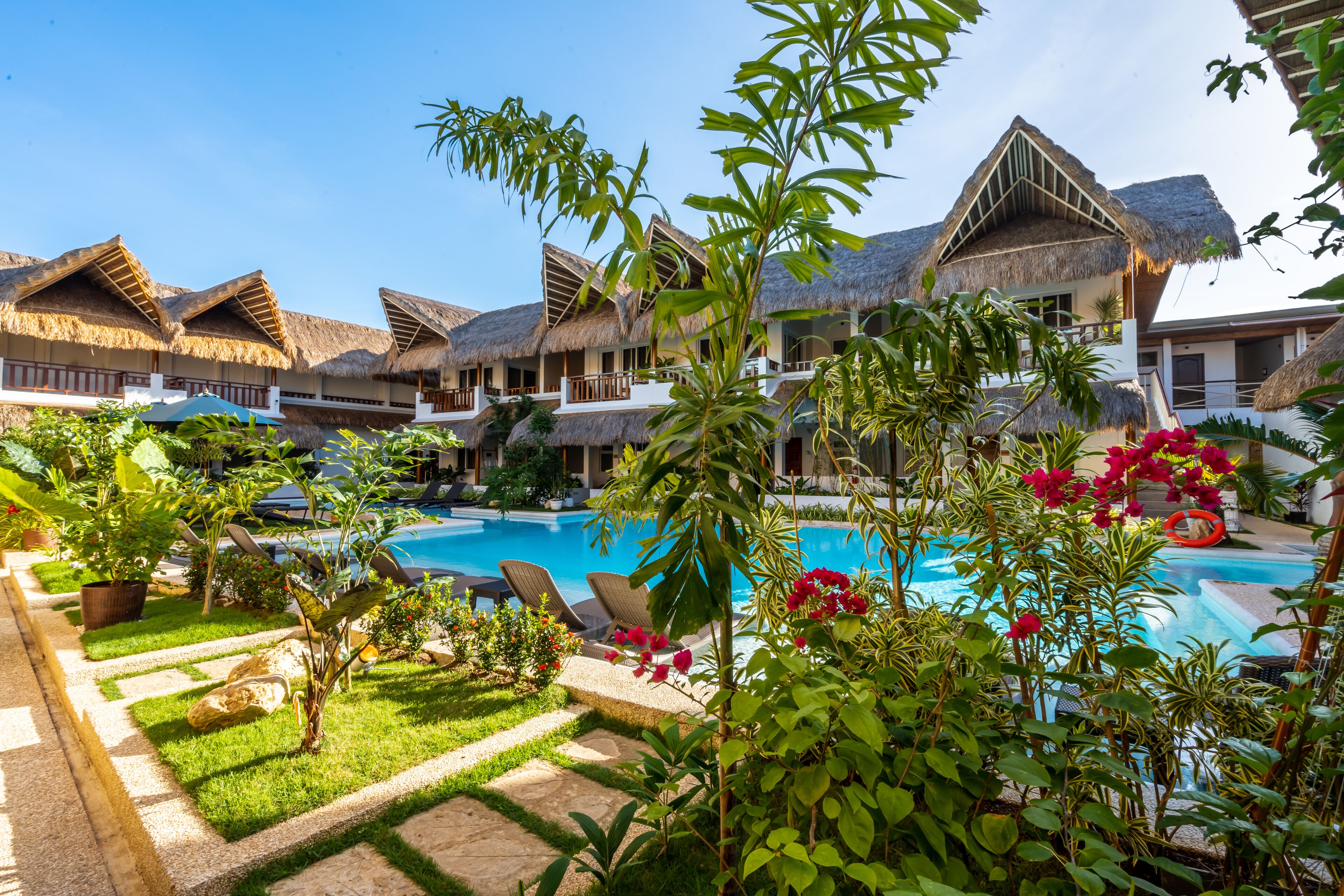 Un resort con bungalós de techo de paja, una piscina y abundante vegetación.
