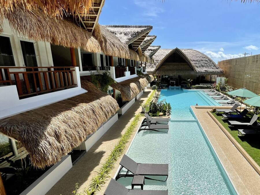 A resort with thatched-roof villas, a swimming pool, and lounge chairs.