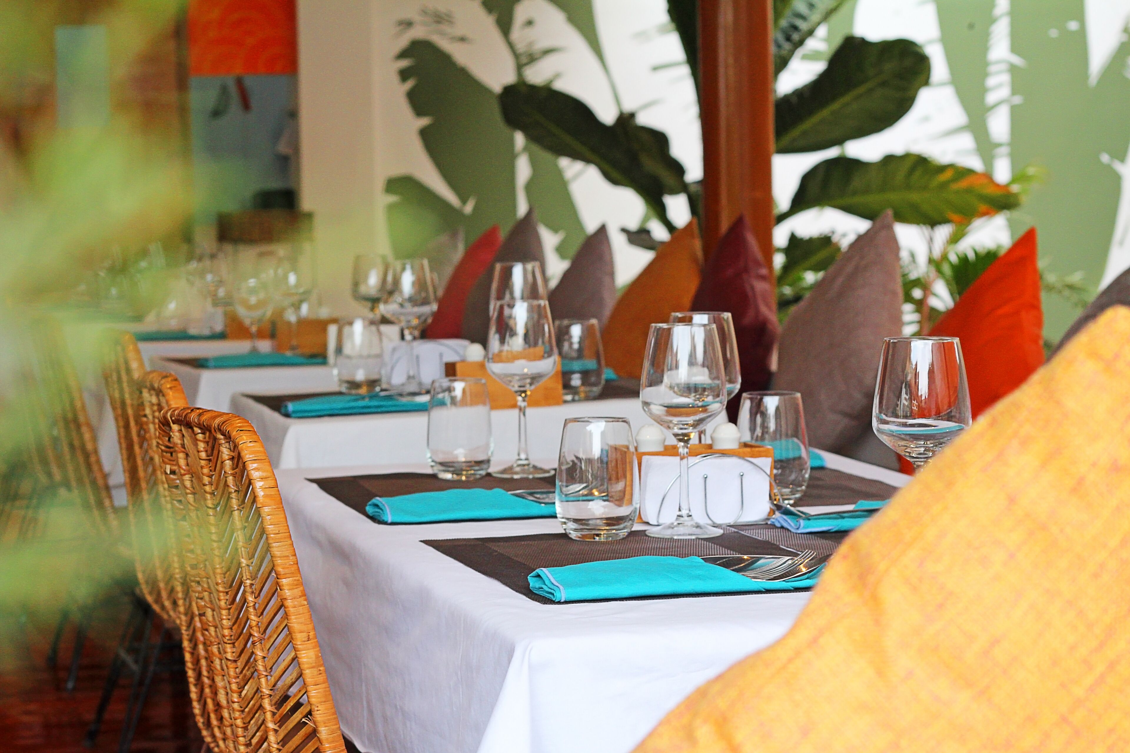Une table de restaurant dressée avec des verres à vin, des verres à eau et des couverts, recouverte d’une nappe blanche et agrémentée de serviettes de couleur turquoise.