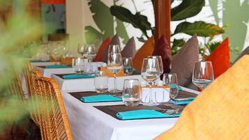 Une table de restaurant dressée avec des verres à vin, des verres à eau et des couverts, recouverte d’une nappe blanche et agrémentée de serviettes de couleur turquoise.