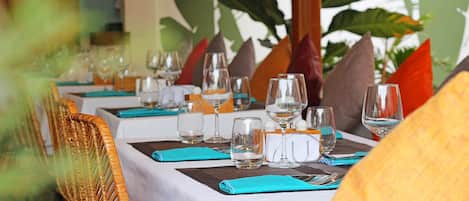 Une table de restaurant dressée avec des verres à vin, des verres à eau et des couverts, recouverte d’une nappe blanche et agrémentée de serviettes de couleur turquoise.