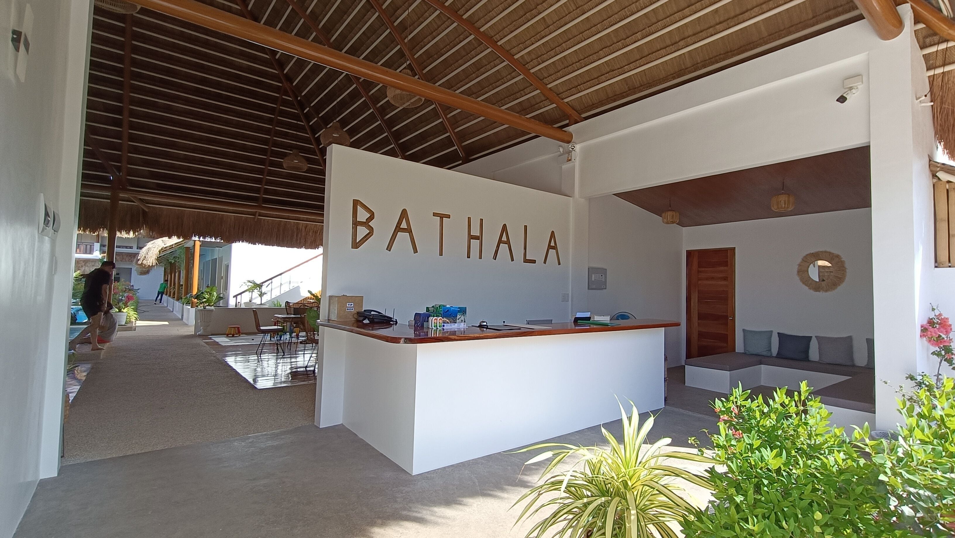 A reception area with a sign reading "BATHALA," a wooden reception desk, a seating area with a sofa, and a thatched roof structure.