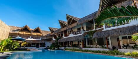 A resort with multiple thatched-roof buildings, a central swimming pool, and lush greenery.