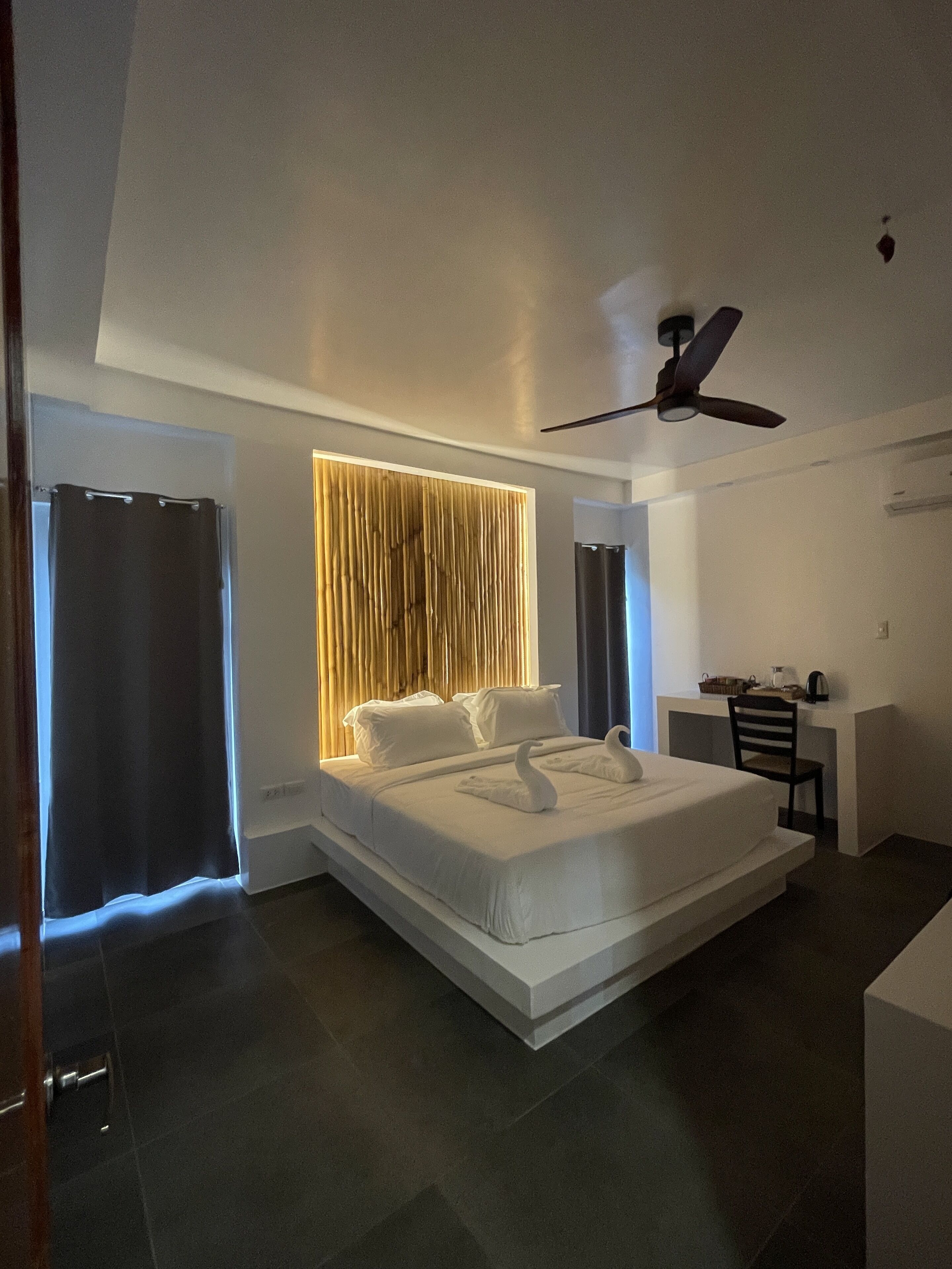 A modern bedroom with a large bed, a desk, and a ceiling fan.