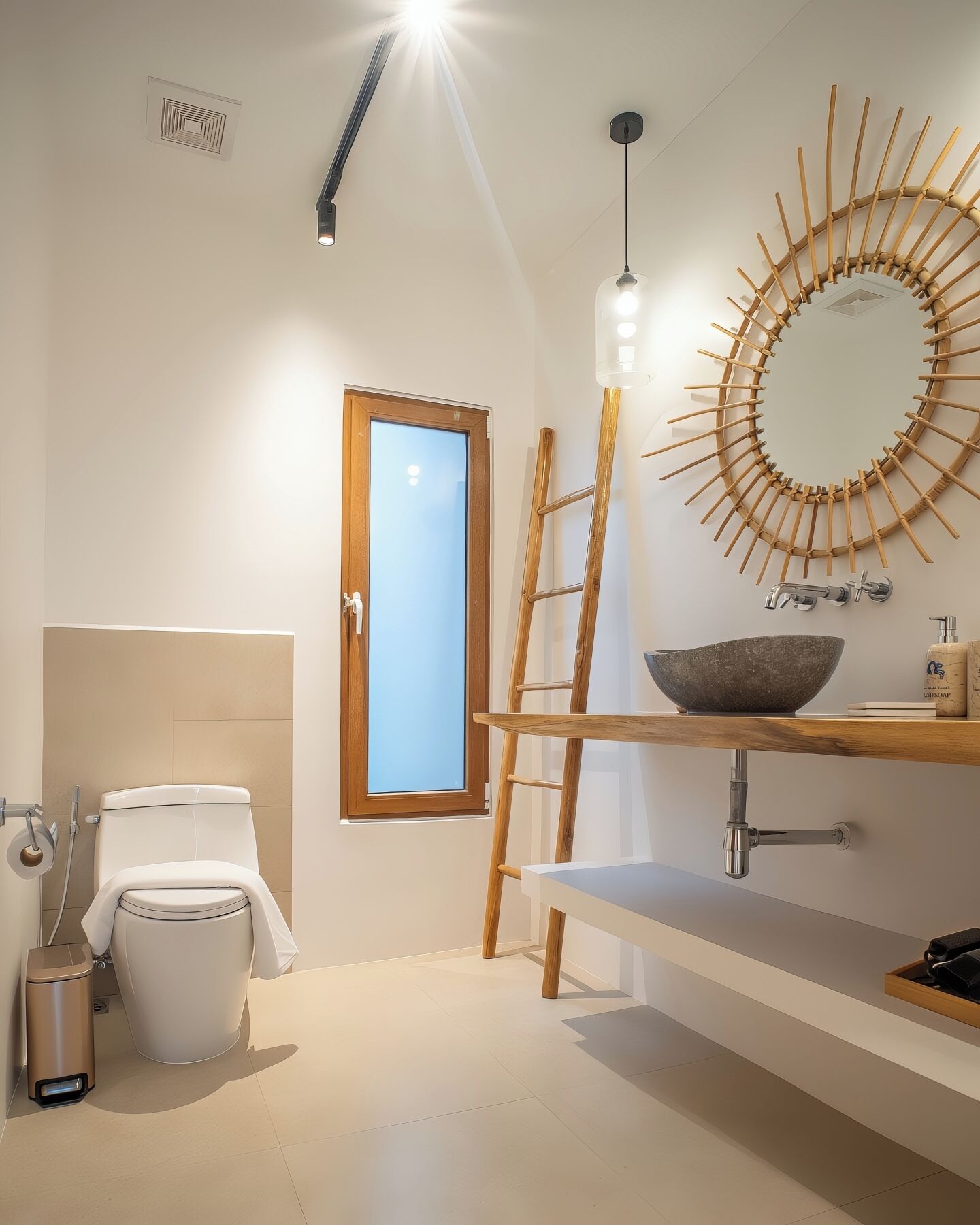 A modern bathroom with a toilet, a sink with a bowl, a wooden ladder, a circular mirror, and a window.