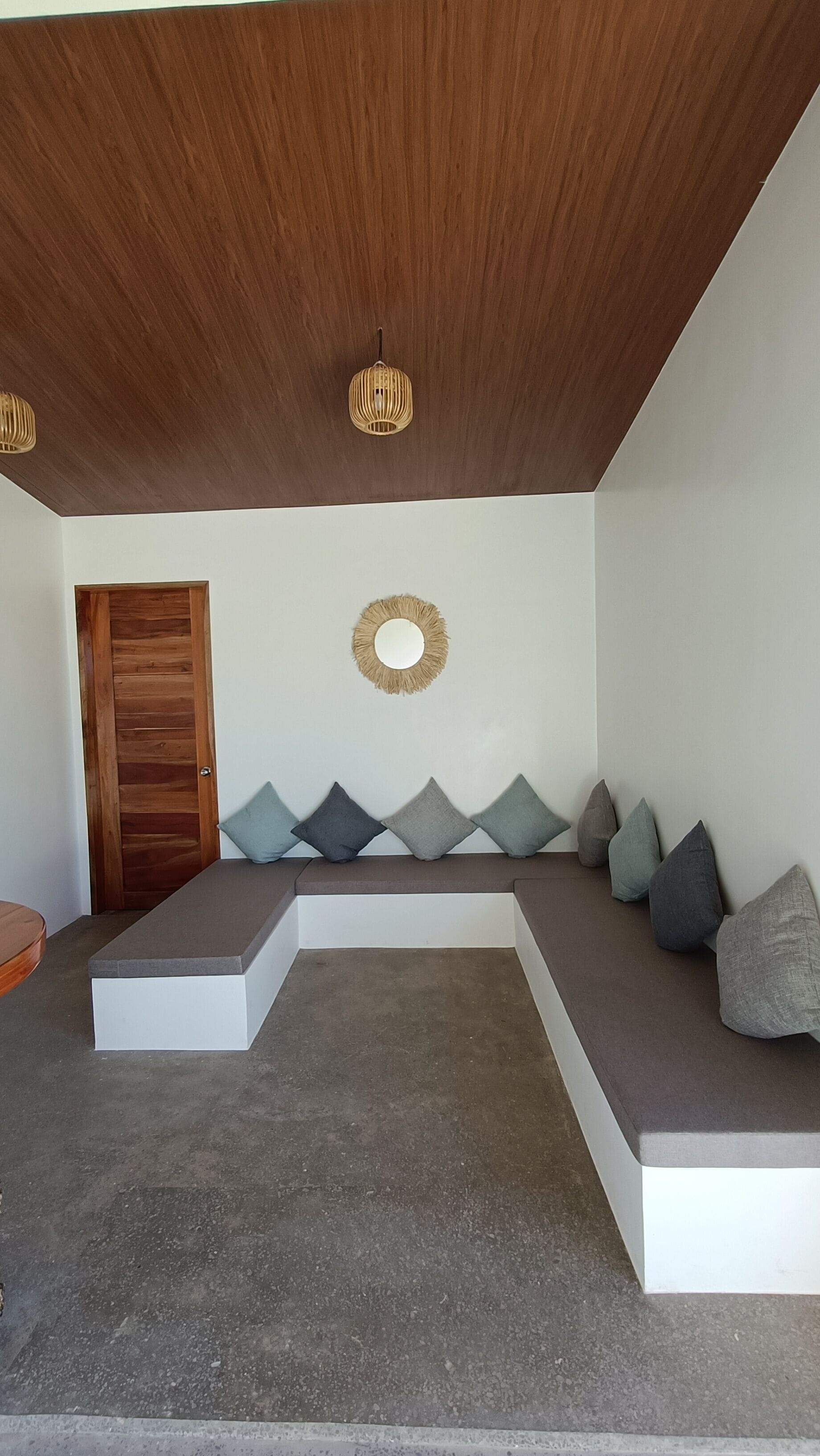 A modern interior with a wooden ceiling, a round mirror, and a bench with cushions.