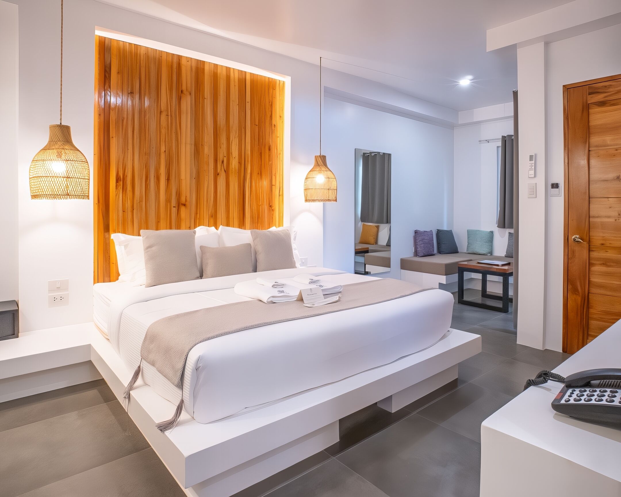 A modern hotel room with a large bed, bedside lamps, a wooden accent wall, and a desk with a telephone.