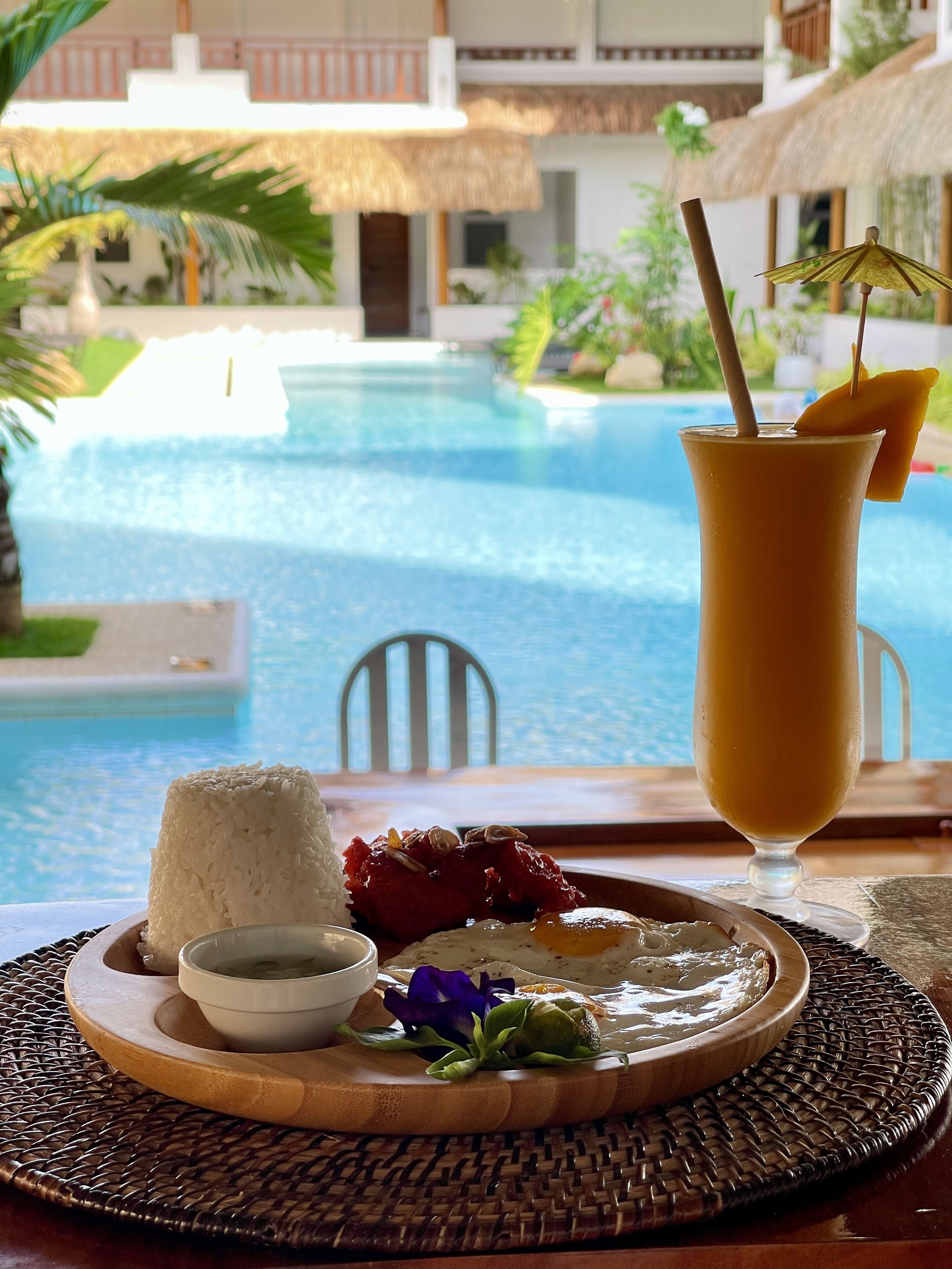 A dining table with a plate of food, a drink, and a view of a pool.