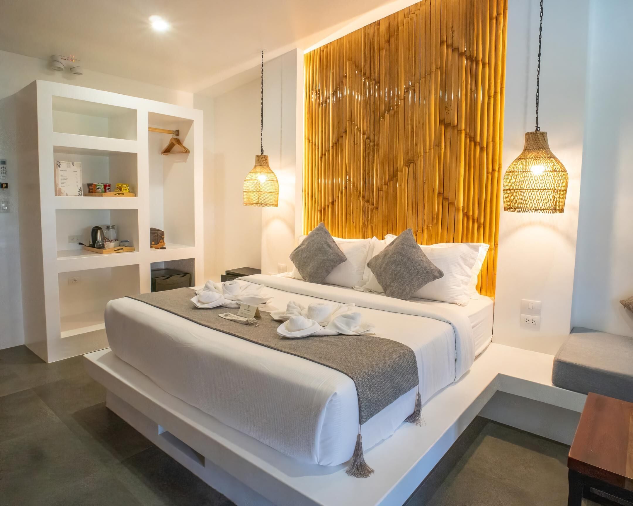 Ein modernes Hotelzimmer mit einem großen Bett, weißen Wänden, einer Wand mit Holzpaneelen und Pendelleuchten.