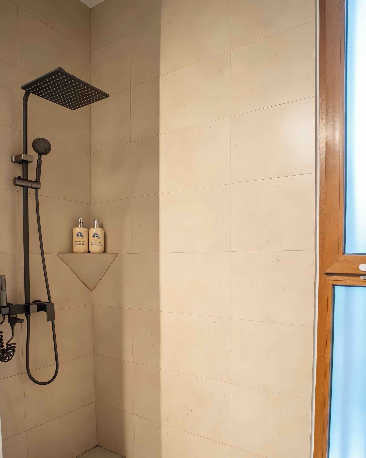 A shower with a square head, a handheld showerhead, and two bottles of shampoo on a shelf.