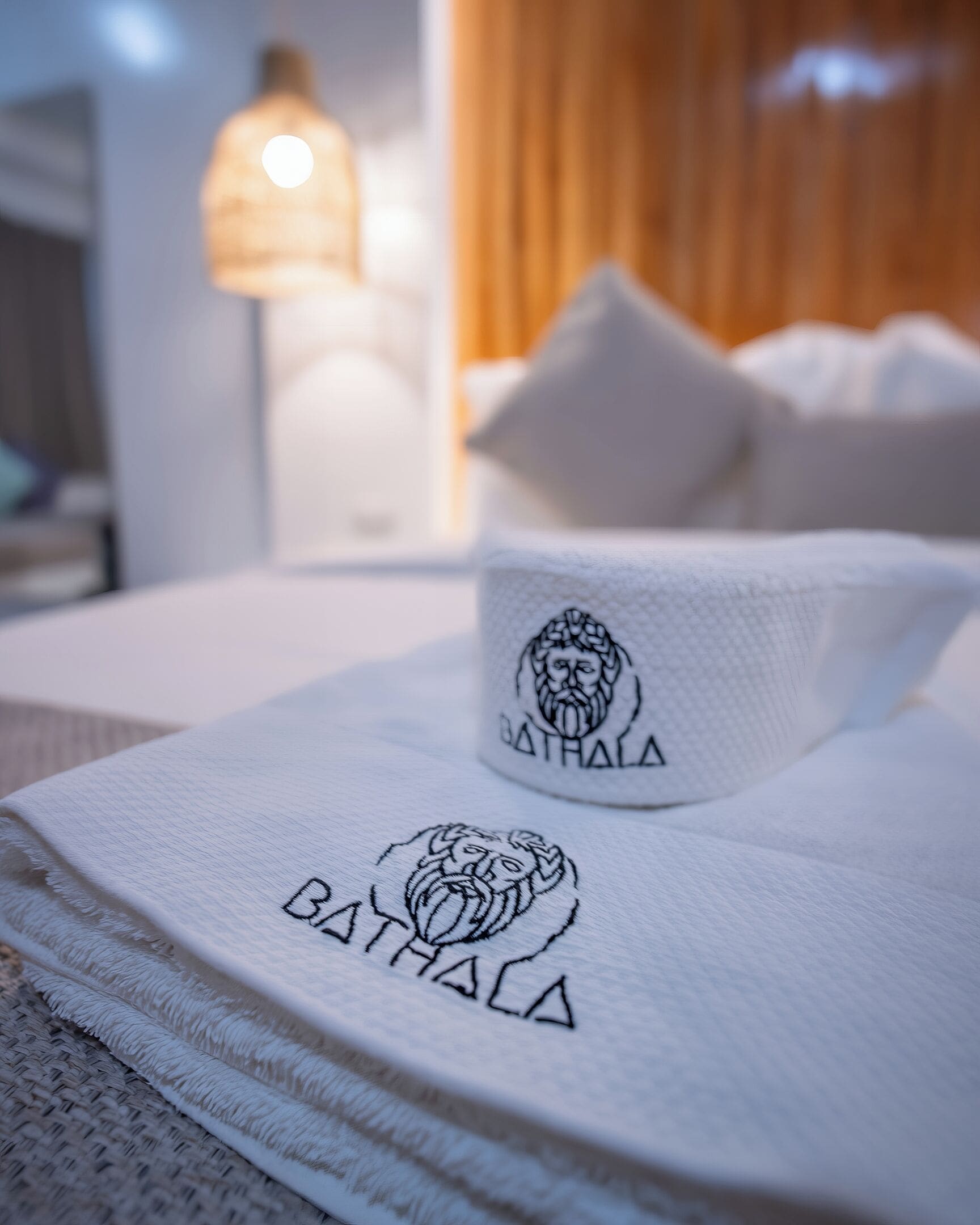 Ett välordnat hotellrum med ett vitt sängöverkast, en handduk med ett lejonmönster och en mugg med en lejonlogotyp.