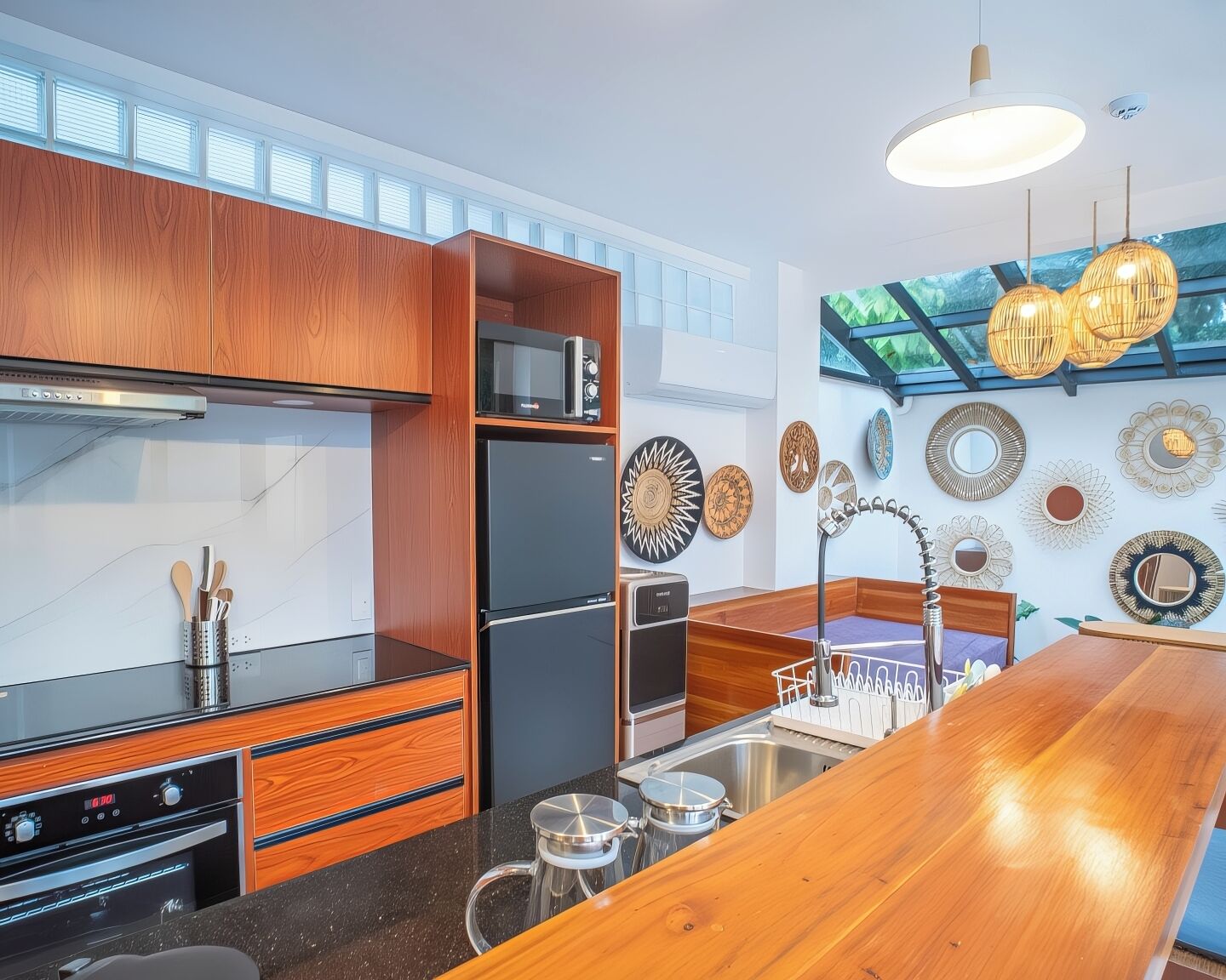 A modern kitchen with wooden cabinets, a black refrigerator, a microwave, and a large window above the sink.