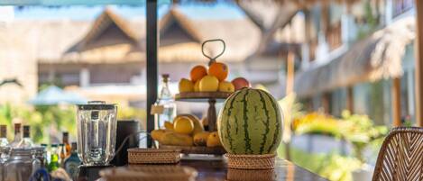 A table with a watermelon, a fruit basket, and a blender.