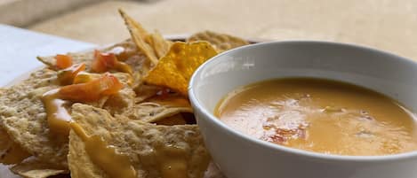 A wooden serving tray with nachos, a bowl of soup, and a pool in the background.