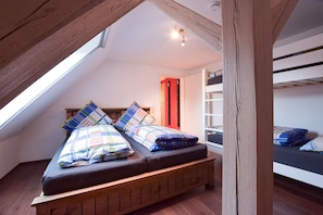 A loft bedroom with a sloped ceiling, a wooden bed frame, a colorful quilt, and a skylight.