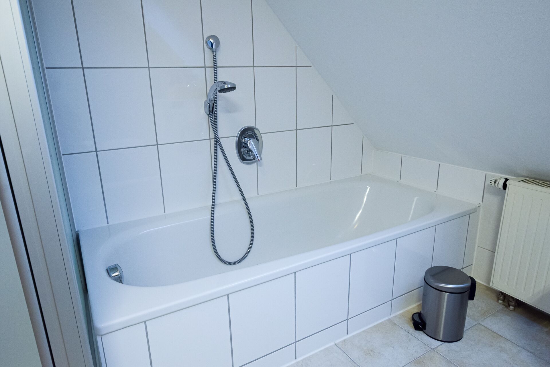 Een moderne badkamer met een witte badkuip, een handdouche en een prullenbak.