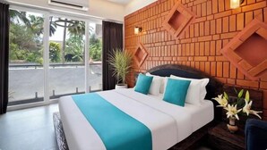 Habitación de hotel con una cama grande, cabecera de ladrillo, una planta en maceta y vistas a palmeras a través de la ventana.