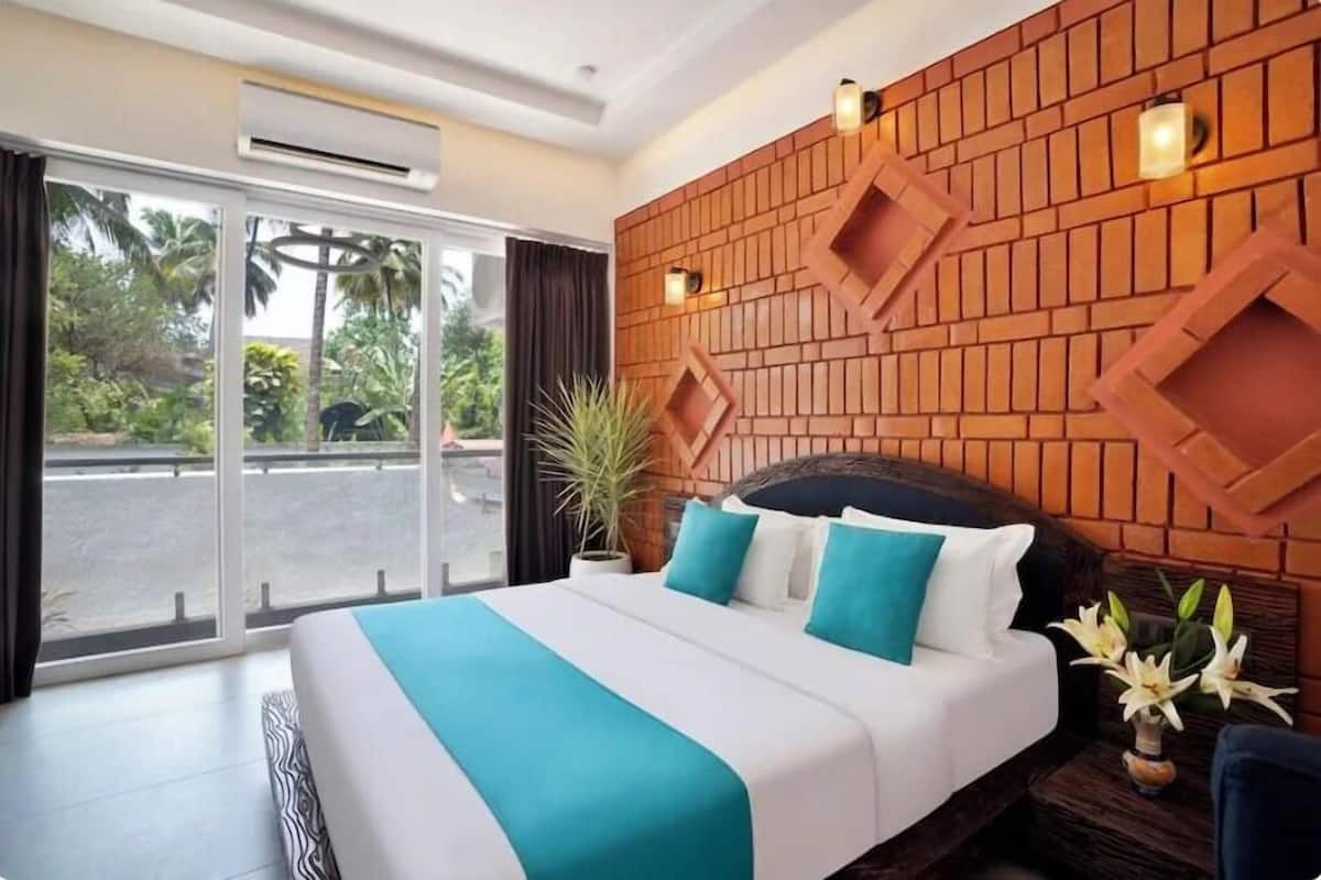 A hotel room with a large bed, a brick-patterned headboard, a potted plant, and a view of palm trees through the window.