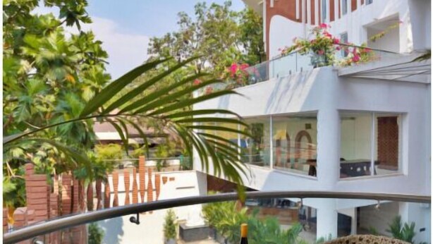 Un espacio exterior moderno con sillas de mimbre y una mesa de vidrio, con vistas a una piscina y un edificio blanco con balcones.