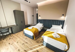 A hotel room with two beds, a desk, and a wardrobe.