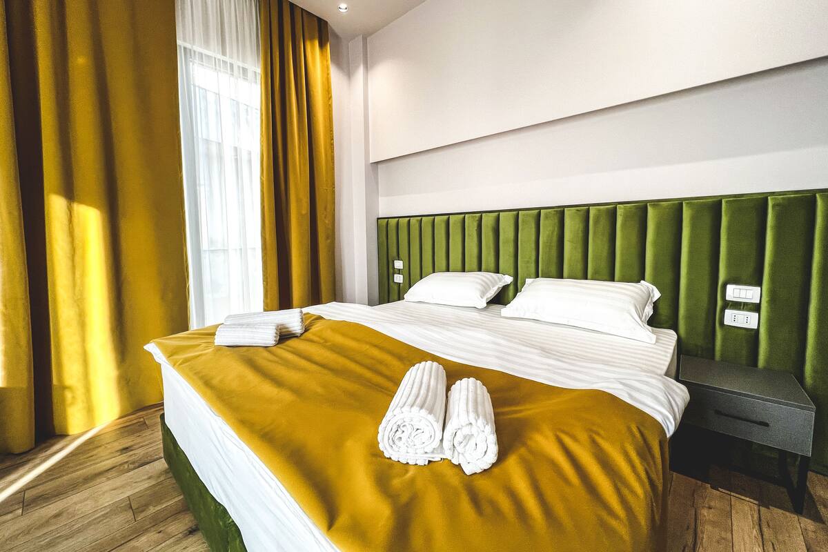A hotel room with a large bed, green headboard, and a wooden floor.